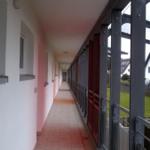 Langgezogener Flur mit Fenstern und Balkon mit Metallgeländer.