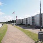Strandpromenade mit Wohnhaus und Leuchtturm im Hintergrund.
