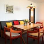 Essbereich mit Holztisch, roten Stühlen und Sofa mit Kissen.