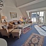 Wohnzimmer mit Ledersofa, Sessel und Teppichen. Glastüren führen auf eine Terrasse.