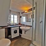 Badezimmer mit Dusche, Waschmaschine und Waschbecken unter Fenster.