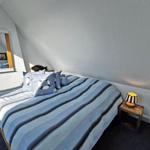 Schlafzimmer mit Bett, Nachttisch und Spiegel an schrägen Wänden.