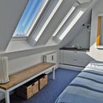 Schlafzimmer mit Dachfenstern, Bett, Schrank und Bank mit Körben.