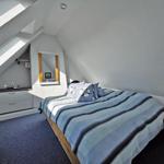 Schlafzimmer mit Dachschrägen, Bett mit blau gestreifter Bettwäsche und Kleiderschrank.