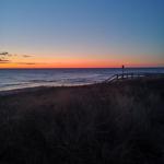 Sonnenuntergang am Meer mit Dünen und Holzbrücke