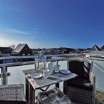 Terrasse mit Tisch, Stühlen und Blick auf Häuser und Hügel.