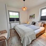 Schlafzimmer mit Doppelbett, Holzboden und zwei Fenstern.