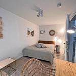 Schlafzimmer mit Bett, Wandregal und Tisch. Tür führt zu Flur.