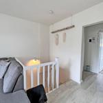 Wohnbereich mit grauem Sofa und weißen Geländern. Hintergrund zeigt einen Durchgang.