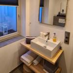 Badezimmer mit Waschbecken, Spiegel und Fenster mit Jalousie.