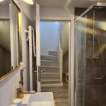 Badezimmer mit Dusche, Waschbecken und Spiegel. Treppe führt nach oben.