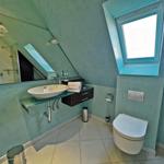 Badezimmer mit Dusche, Waschbecken und Toilette unter Dachschräge.