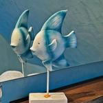 Zwei Fischfiguren auf Holzsockel vor blauer Wand