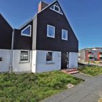 Haus mit schwarzem Dach und weißer Fassade, Eingangstür und Fenster mit Vorhängen.