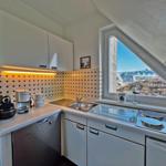 Küche mit Spüle, Herd und Waschmaschine unter Dachschrägen mit Blick auf Außenbereich.