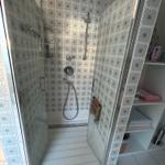 Dusche mit Glaswand und Mosaikfliesen, daneben Regal mit Handtüchern.