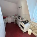 Küche mit rotem Boden, weißen Geräten und Fenster mit Vorhang.