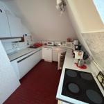 Küche mit rotem Boden und weißen Schränken unter schrägem Dach