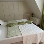 Schlafzimmer mit Doppelbett, Kleiderschrank und Fenster mit grünen Vorhängen.