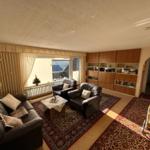 Wohnzimmer mit Ledersofa, zwei Sesseln, Teppich und Holzmöbel.