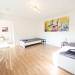 Zimmer mit zwei Betten, Holzboden und Wandbild mit Kränen.