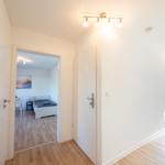 Flur mit Tür zu Schlafzimmer und Fenster. Holzboden und weiße Wände.