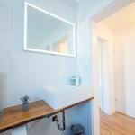 Badezimmer mit Waschbecken, Spiegel und Holzregal.