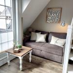Ein Sofa mit Kissen, Tisch und Wanddekoration in einem Raum mit Dachschräge und Fenster.