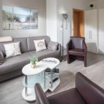 Wohnzimmer mit Sofa, zwei Sesseln und Tisch. Wandbild zeigt Strand.