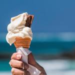 Eine Hand hält einen Eistüten mit Schokoladenstückchen vor dem Meer.