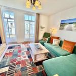 Wohnzimmer mit grünem Sofa, buntem Teppich und Fenstern zum Balkon.