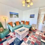 Ein Wohnzimmer mit grünem Sofa, gemustertem Teppich und Wandbildern.