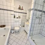 Badezimmer mit Badewanne, Dusche und Toilette. Weiße Fliesen und dekorative Bordüre.