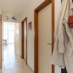 Flur mit Tür zu Wohnzimmer, Mantel und Handtasche hängen an Tür.