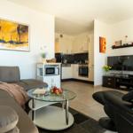 Wohnzimmer mit Sofa, Couchtisch und Küche im Hintergrund.