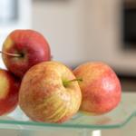 Vier rote Äpfel auf einer Glasplatte in der Küche.