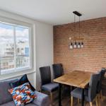 Essbereich mit Holztisch, vier Stühlen und Backsteinwand. Große Fenster mit Blick nach draußen.