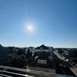 Blick von Balkon auf städtische Umgebung unter blauem Himmel mit Sonne.