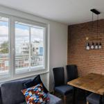 Raum mit Sofa, Tisch und Stühlen. Backsteinwand und Fenster mit Blick.