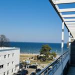 Blick von Balkon auf Strand und Meer mit Parkplatz und Gebäude.