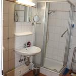 Badezimmer mit Dusche, Waschbecken und Toilette. Fliesenboden und Spiegelschrank.