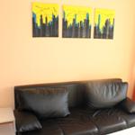 Schwarzes Sofa mit Kissen, Wand mit drei Kunstwerken, orange Vorhänge.