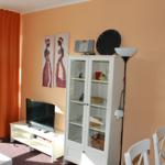 Wohnzimmer mit Fernseher, Glasvitrine und orangefarbenen Vorhängen.