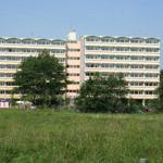 Hochhaus mit mehreren Stockwerken und Fenstern, umgeben von Bäumen und Gras.