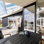 Terrasse mit Tisch, Stühlen und Liegestuhl. Glasfront und Dach überdacht.