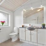 Badezimmer mit Waschbecken, Toilette und Fenster mit Blumen.
