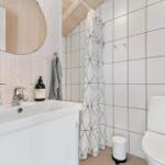 Badezimmer mit Waschbecken, Dusche und Toilette. Holzwand, Spiegel und Duschvorhang.