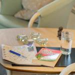 Runde Tisch mit Buch, Kreuzworträtsel und Glas Wasser.