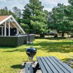 Haus mit Grill und Picknicktisch auf grünem Rasen vor Bäumen.