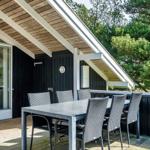 Terrasse mit Tisch und Stühlen unter Dach, umgeben von Bäumen und einer Holzwand.